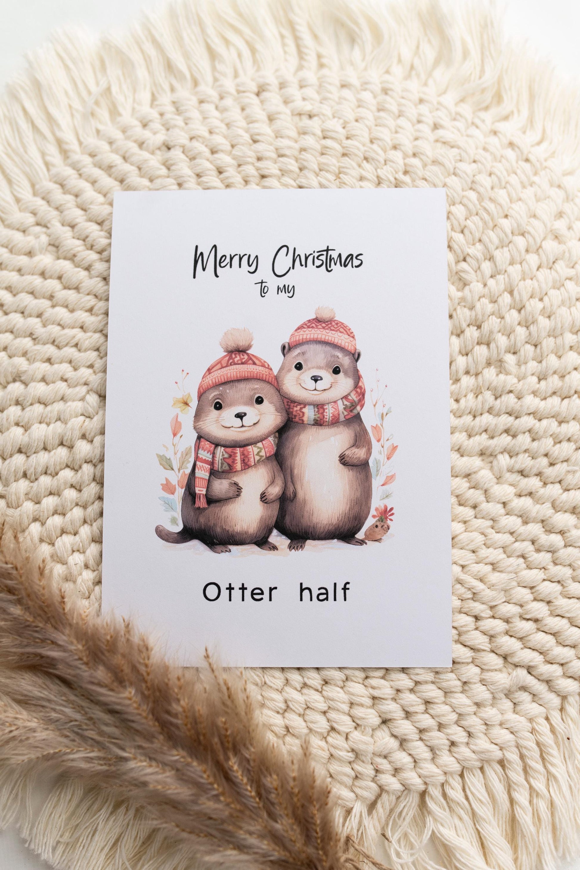 Süße Weihnachtskarte mit einem Otterpaar mit Wintermütze und Schal im Aquarelllook und dem Text "Merry Christmas to my Otter half". Die Karte ist im A6 Format und hat eine Blanko-Rückseite für ihre persönliche Nachricht.